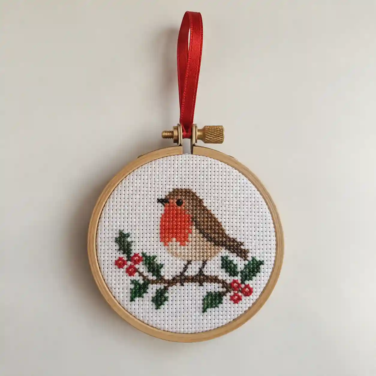 A small finished cross-stitch piece mounted into a hanging ornament with a ribbon loop