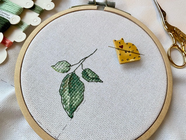 A leaf stitched in a hoop, surrounded by floss and scissors