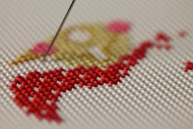 A needle mid-stitch on a piece of red cross-stitch work
