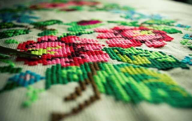 A floral cross-stitch piece in progress, held mid-stitch