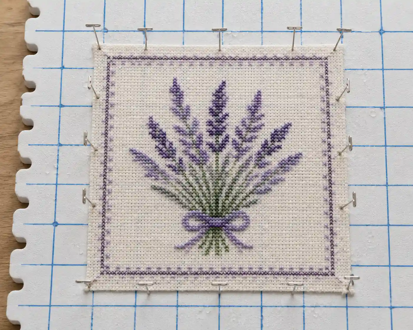 A finished cross-stitch piece pinned out square on a blocking board