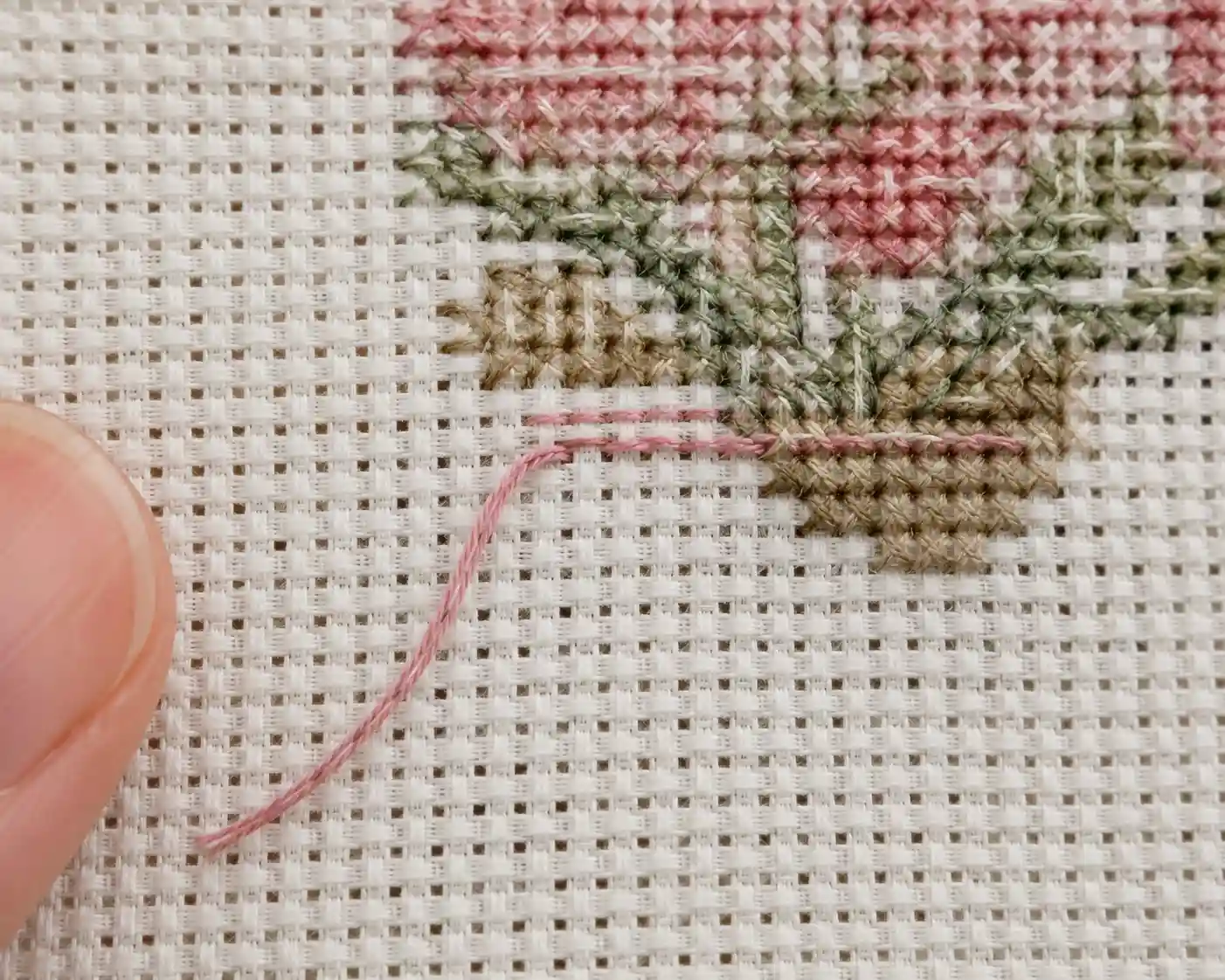 A close-up of the back of a cross-stitch piece showing a thread tail woven in without a knot