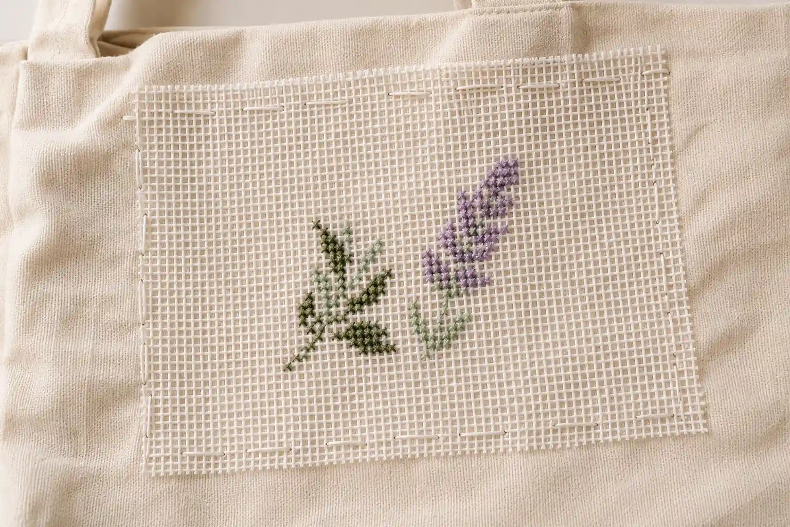 Waste canvas basted onto a canvas tote bag with a small floral motif stitched through it