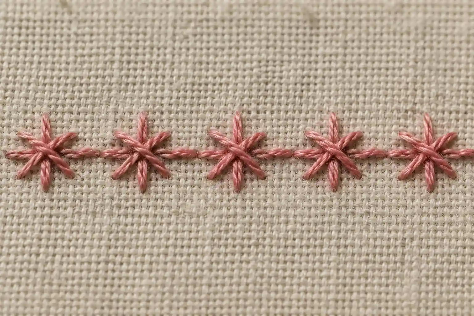 A row of raised, star-shaped Smyrna cross stitches in pink thread